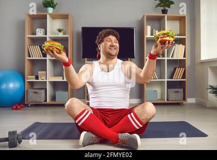 Excited millennial man with chubby body holding fast food burger in two hands Stock Photo
