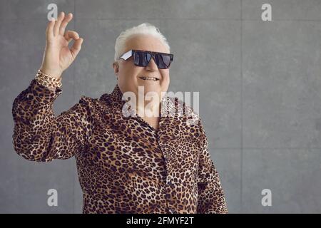 Happy rich chubby senior man in leopard shirt, gold bracelet and glasses doing Okay gesture Stock Photo