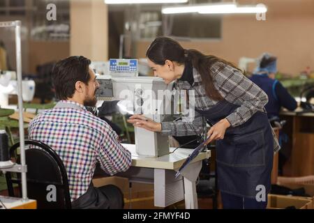 Two shoe factory workers talking at a table with an industrial shoe sewing machine Stock Photo