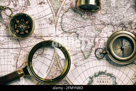 Telescope, magnifying glass and compass on an old world map. Stock Photo