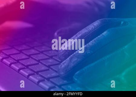Cybercriminal, hands in gloves on laptop keyboard, photo toned in neon light. Stock Photo