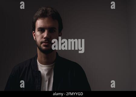 Portrait of a young bearded Spanish male in casual clothes against a black background Stock Photo
