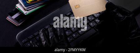 Burglar with a stolen credit card. Hands in glove on laptop keyboard with credit card. Stock Photo