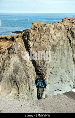 Father and son climb on the rock formations at Fauskasandur, a black sand beach, in east Iceland. Stock Photo