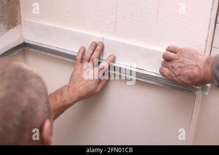 Stylish trendy white ceramic tiles on the kitchen wall. Hands in the process of laying white rectangular tiles on the bathroom wall. Renovation of apa Stock Photo