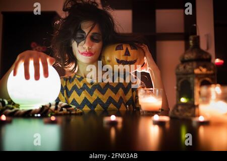 Halloween Witch with pumpkin and magic lights. Young and funny girl with halloween make up and costume ready for party. Stock Photo