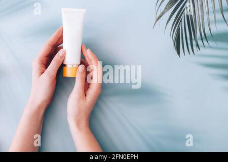 Hands holding tube with skincare cosmetic lotion cream on blue background with palm shadows on it Stock Photo