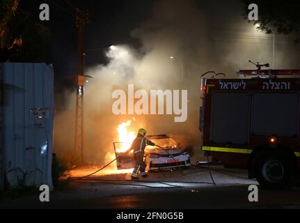 Lod, Israel. 12th May, 2021. An Israeli firefighter works near a burning police car in Lod, central Israel, on May 12, 2021. Israeli police announced on Wednesday that a night curfew will be imposed in Lod, where clashes between Arabs and Jews have been spiraling for days. Credit: Muammar Awad/Xinhua/Alamy Live News Stock Photo