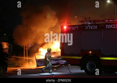 Lod, Israel. 12th May, 2021. An Israeli firefighter works near a burning police car in Lod, central Israel, on May 12, 2021. Israeli police announced on Wednesday that a night curfew will be imposed in Lod, where clashes between Arabs and Jews have been spiraling for days. Credit: Muammar Awad/Xinhua/Alamy Live News Stock Photo