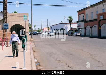 Masked old man walking alone on a sidewalk in a near empty downtown Calexico, California during the Covid-19 pandemic; elderly gentleman all alone. Stock Photo