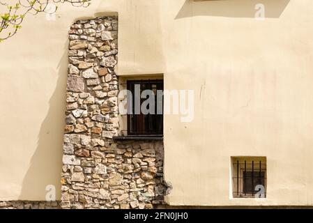 Plastered wall with masonry. Combinations of old stone and plastered walls with windows. Windows with bars in an old house. Stock Photo