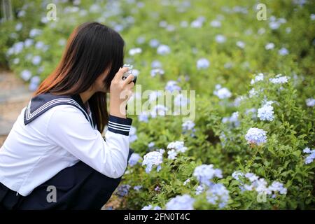 Asian school girl with camera taking photo a flowers in garden Stock Photo