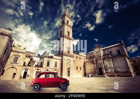 Historic church with a bell tower and old small red car. Small red car parked in front of the last century is the Basilica Church of the Holy Cross in Stock Photo