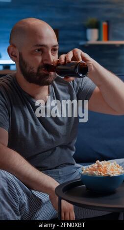 Upset pro gamer sitting in front of television losing soccer video games holding wireless controller, joystick. Frustrated man for gaming over drressing in pajama relaxing playing online competition Stock Photo