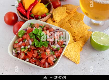 Close up of salsa Roja traditional Mexican sauce with ingredients for making and light beer. homemade recipe Pico de Gallo with nachos. Stock Photo