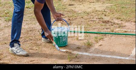 Drawing white lines in a cricket pitch, male hands with a brush and white paint, painting straight lines on the ground. preparation for the softball c Stock Photo