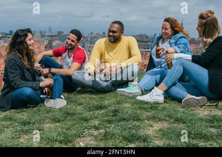 Happy interracial friends sitting in a park talking, laughing and drinking beer Stock Photo