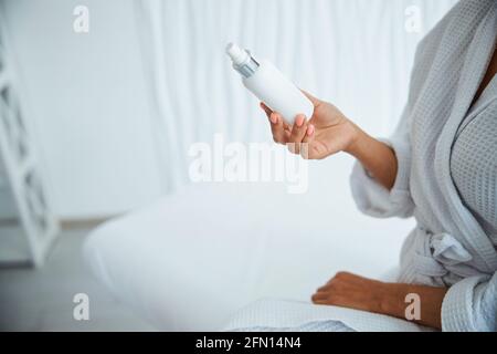 Female in a waffle weave bathrobe holding a new skincare product Stock Photo