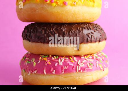 three Berliners donut pink yellow chocolate with a sprinkle on a pink background leit stack on top of each other with a copyspace. Stock Photo