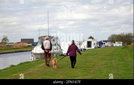 A senior couple walking their dog on a public footpath by Thurne Dyke on the Norfolk Broads at Thurne, Norfolk, England, United Kingdom. Stock Photo