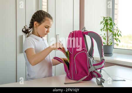 Schoolgirl in school clothes preparing for school and collecting notebook in a briefcase. Stock Photo