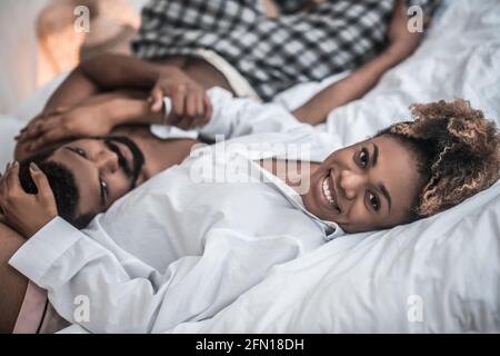 Joyful african american woman hugging husband on bed Stock Photo