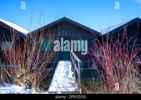 View of a small snowed-in bridge to a boathouse on a lake. Stock Photo