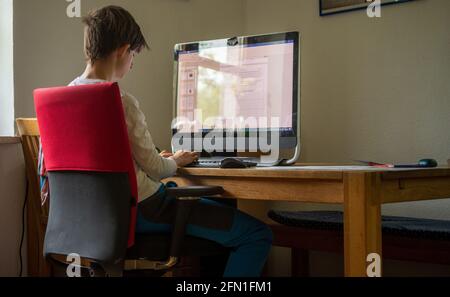 A teenager sits at home doing homework on his computer Stock Photo