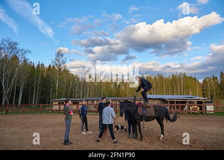 Russia, Moscow region, May 2021. A teenage girl is studying horse riding at an equestrian school. A girl stands on the back of a horse.