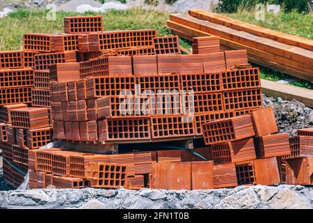 A pile of red perforated clay bricks and wooden beams – materials at construction site. Stock Photo