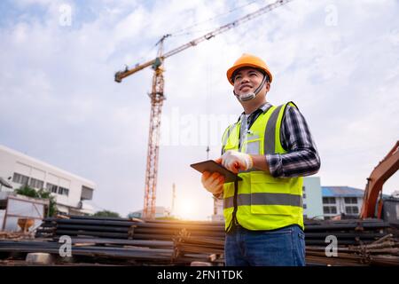 male construction engineer. Architect with a tablet computer at a construction site. Asian young man looking, building site place on background. Const Stock Photo