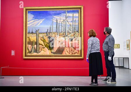 Brighton UK 13th May 2021 - Co-curators Sara Cooper and Andy Friend with the famous Oppy Wood painting (on loan from the Imperial War Museum ) by John Nash at the Towner Eastbourne as they prepare to present the first major exhibition of John Nash works in 50 years, as galleries across England reopen after lockdown. Towner Eastbourne presents the most comprehensive exhibition of work in over 50 years by John Nash, one of the most versatile and prolific artists of the 20th century. Credit: Simon Dack/Alamy Live News Stock Photo