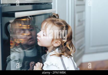 Child leaned against oven. Little girl is waiting for the cookies to be cooked Stock Photo