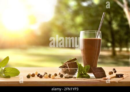 Milk chocolate shake with portions of dark chocolate and mint on wooden table in nature Stock Photo