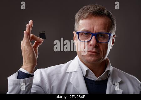 Scientist or forensics expert in a white lab coat holding up an SD Card with digital data in his hand during an investigation over a dark background Stock Photo