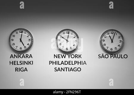 Many wall clocks on the white wall of business office showing time of different cities of the world Stock Photo