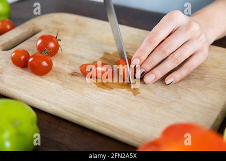 cropped view of woman cutting red cherry tomatoes on wooden chopping board Stock Photo