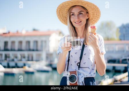 Young blonde woman on a summer day holding an instant photo in her hands and an ice cream cone. Stock Photo