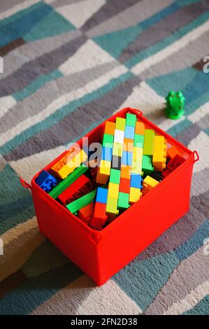 POZNAN, POLAND - Mar 20, 2016: Colorful Lego Duplo plastic build bricks stored in a red storage container laying on a carpet floor in high angle view. Stock Photo