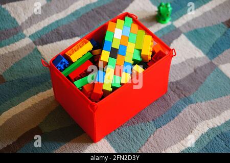 POZNAN, POLAND - Mar 19, 2016: Colorful Lego Duplo plastic build bricks stored in a red storage container laying on a carpet floor in high angle view. Stock Photo