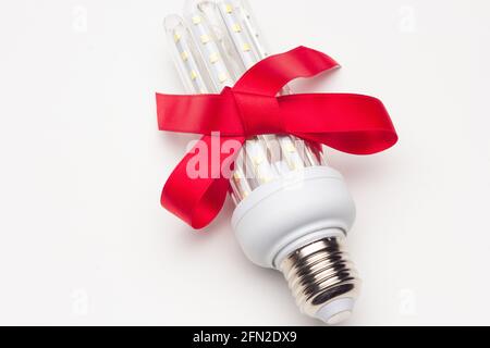 Energy-saving light bulb with a red ribbon; saving is a gift in addition to preventing global warming; ecology is a gift for our descendants. Stock Photo