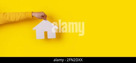 hand holding house over yellow background, construction concept, panoramic mock-up Stock Photo