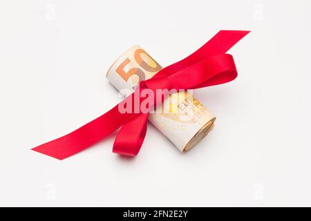 Roll of Euro banknotes surrounded by a red ribbon and a pretty bow. Colorful ribbon surrounding euro banknotes. Give money as a gift. To donate to an Stock Photo