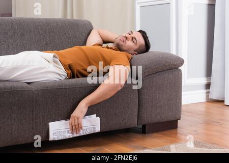 young man sleeping on couch while holding newspaper Stock Photo