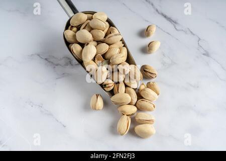 Pistachio shovel in the shell close up on a white marble background. Isolated. Stock Photo