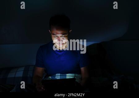 man using tablet to reading in bed and turning off the lights before getting some shut-eye sleep. working on bed Stock Photo