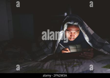 man using tablet to reading in bed and turning off the lights before getting some shut-eye sleep. working on bed Stock Photo