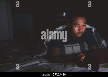 man using tablet to reading in bed and turning off the lights before getting some shut-eye sleep. working on bed Stock Photo
