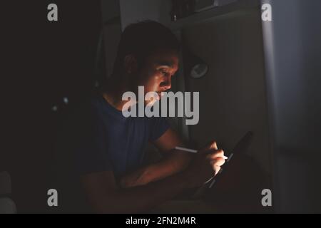 man using tablet to reading in bed and turning off the lights before getting some shut-eye sleep. working on bed Stock Photo