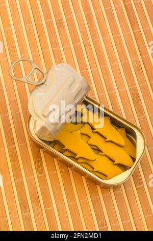 Tinned fish can with small wood figures of fish. For packed in like sardines, no room to move, tight fit, squashed together, overcrowded abstract. Stock Photo